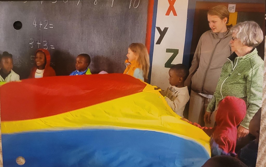 Kinder stehen um ein Schwungtuch in Regenbogenfarben.